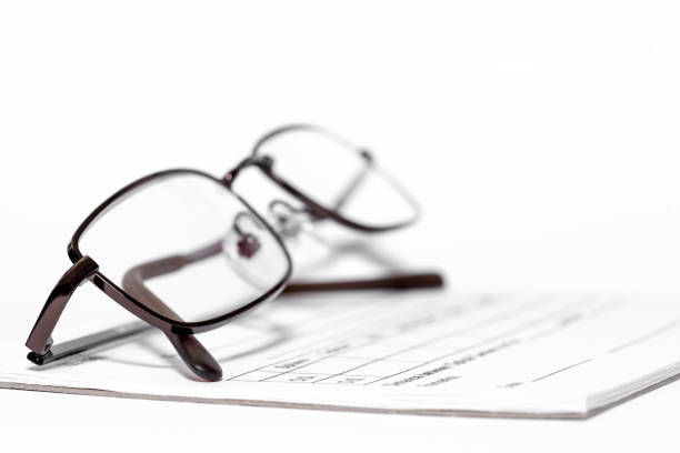Close up color image depicting a young adult male, in his 30s and of caucasian ethnicity, reading a newspaper. He is wearing blue framed trendy spectacles, and is concentrating with a look of extreme focus on the newpaper in front of him. He has a shocked or surprised expression on his face, as if he has read something very shocking or contoversial. His eyes are wide, showing his surprise. The newspaper occupies the lower portion of the frame and is blurred out of focus. The man has a ginger beard and moustache. Lots of room for copy space in the plain white background.