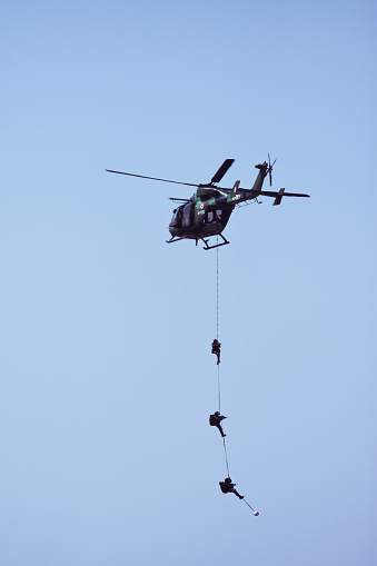 Bangalore, Karnataka, India - 02/17/2017 : Taken this picture at Aero India in Bangalore, India where this Indian Army helicopter performing daredevil stunts in front of spectators. This is a team of Indian soldiers hanging in under the Dhruv helicopter demonstrating the way of extracting soldiers out of war zone.