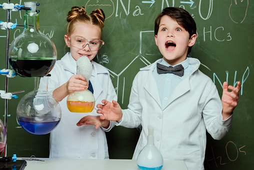little kids in white coats with chalkboard behind in laboratory, scientists kids team concept