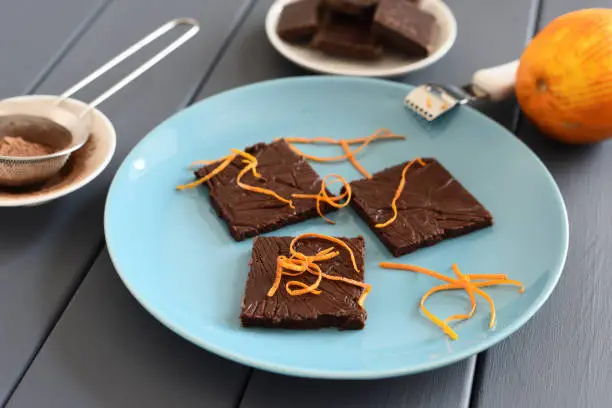 Healthy homemade dark chocolate bars with orange rind on turquoise plate closeup