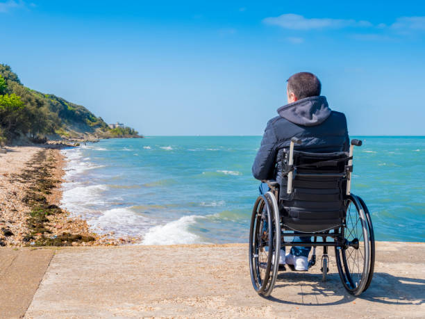 Back of disabled man in wheelchair at beach Back of alone disabled young man in wheelchair at beach. paraplegic stock pictures, royalty-free photos & images