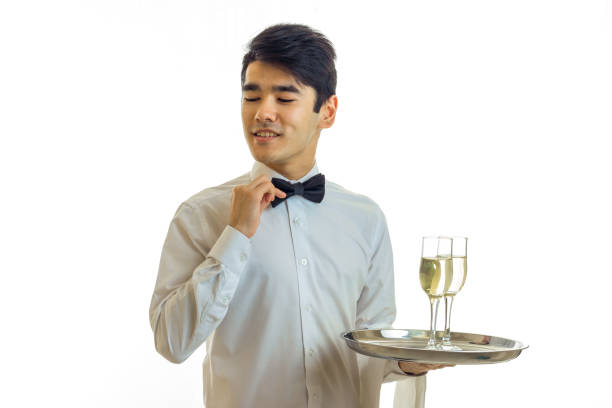 charming young waiter in a white shirt holding a tray with glasses of wine and adjusts his bow tie hand