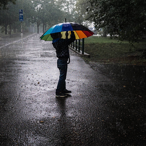 istock Side View Of Boy Standing With Umbrella On Road During Rain 692058693
