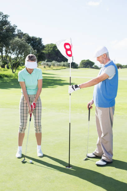 istock Golfer holding eighteenth hole flag for partner putting ball 692081350