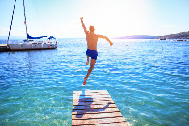 Cheerful man jumping into water Young man jumping into water from a pier. people jumping sea beach stock pictures, royalty-free photos & images