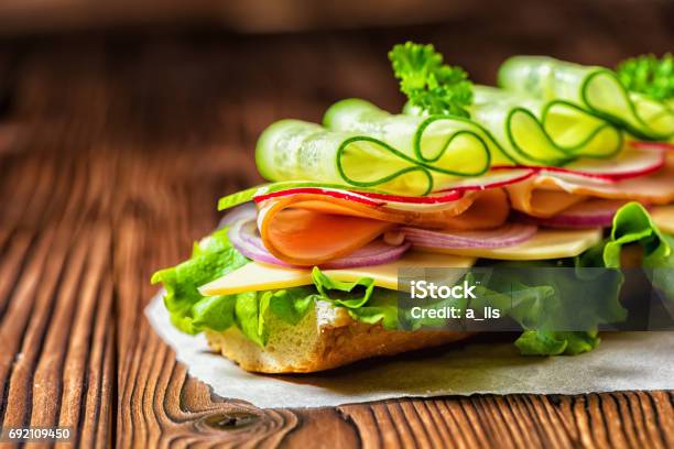 Close Up Of Sandwich With Ham Cheese Bacon Radish Lettuce Cucumbers And Onions On Paper Wooden Background Stock Photo - Download Image Now