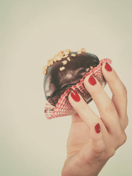 Woman hand holding chocolate cupcake about to bite