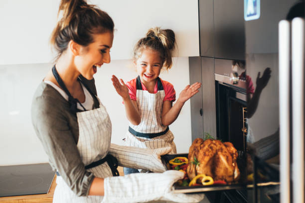 Mother taking the dinner out of the oven Little girl watching her mother taking the turkey out of the oven. apron photos stock pictures, royalty-free photos & images