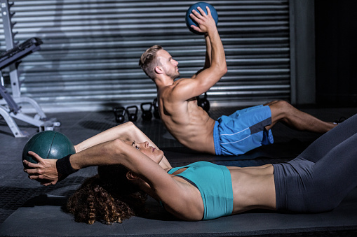 Muscular couple doing abdominal crunch with a ball