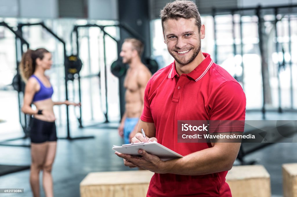 Smiling muscular trainer writing on clipboard Portrait of a muscular trainer writing on clipboard Fitness Instructor Stock Photo