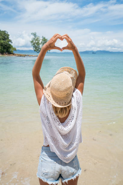istock Woman making heart shape frame on tropical beach landscape 692175764