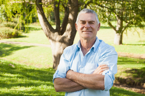 Portrait of a content mature man standing with arms crossed at the park