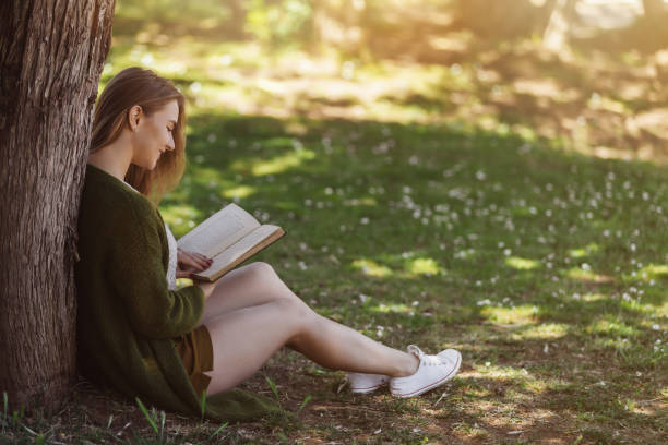 istock Beautiful young woman reading book in the forest 692244866