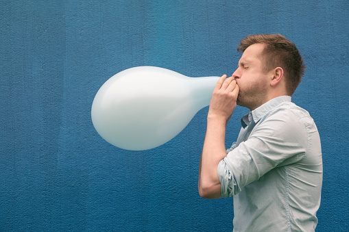 Man blowing up a balloon on ble background