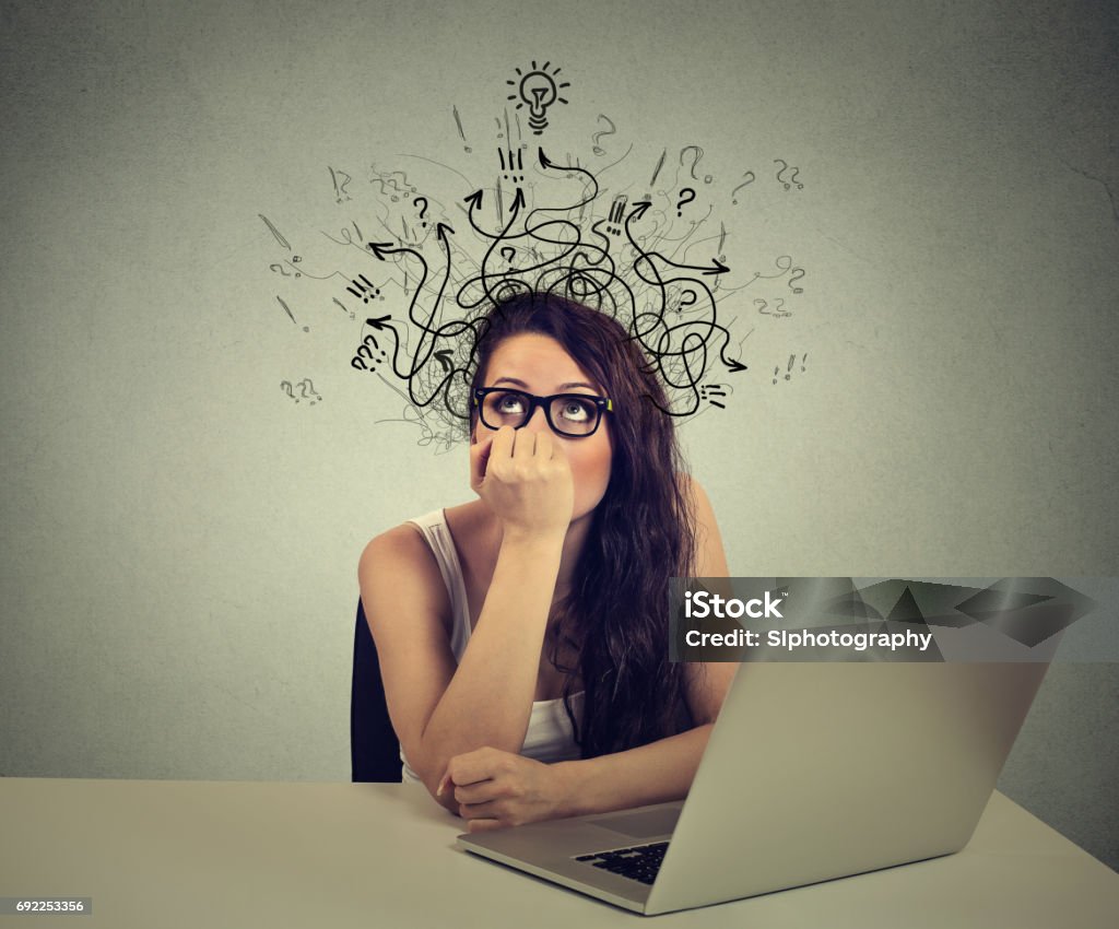 woman with thoughtful expression sitting at a desk with laptop with lines arrows and symbols coming out of her head Young woman with thoughtful expression sitting at a desk with laptop with lines arrows and symbols coming out of her head Attention Deficit Hyperactivity Disorder Stock Photo