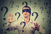 blindfolded man stretching his arms out walking through many question marks