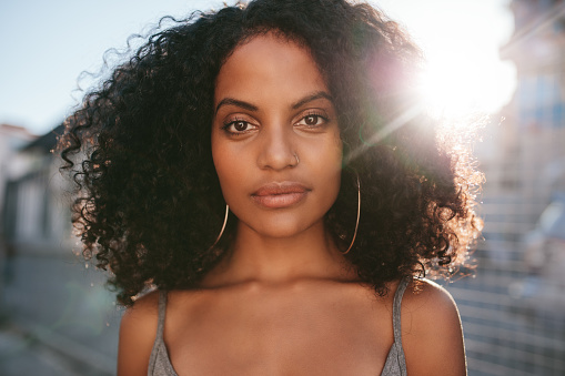 Close up portrait of beautiful young african woman with curly hair. Afro american female standing outdoors.