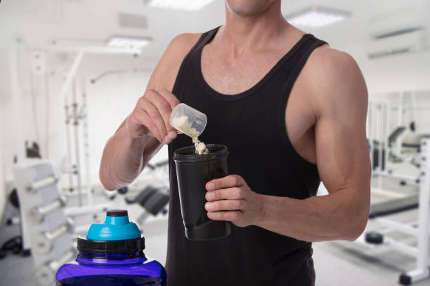 Weight gain. Man put whey protein with amino acids bodybuilding dietary supplement in shaker. Fitness, muscle recovery and sport concept. stock photo