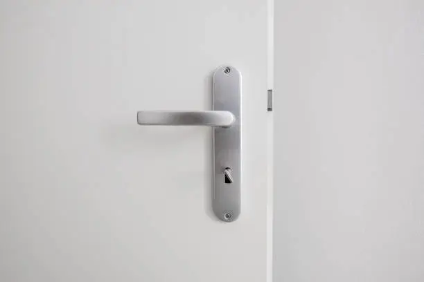 Photo of metal door handle with key on white door