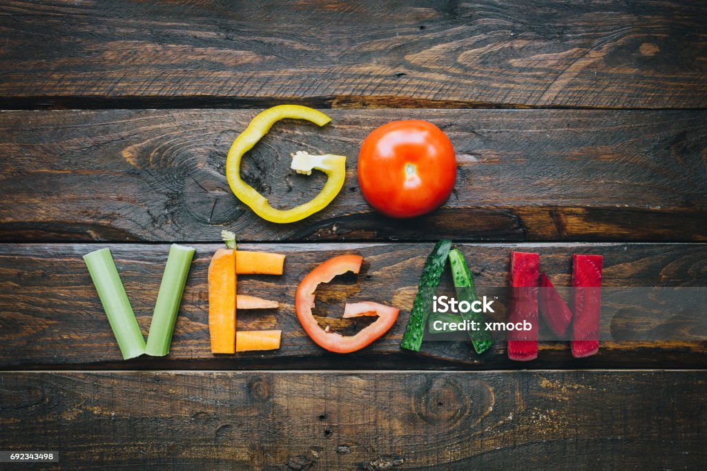 Go vegan fresh vegetables flat lay lettering on dark wooden table top view. Nutrition meal ingredients concept. Nice cooking postcard, poster, banner. Vegan Food Stock Photo