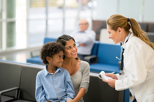 Happy family doctor talking to a mother and son at the hospital - healthcare and medicine concepts