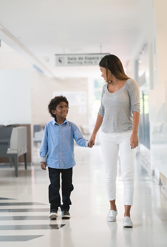 Mother and son walking at the hospital holding hands and looking happy - healthcare and medicine concepts