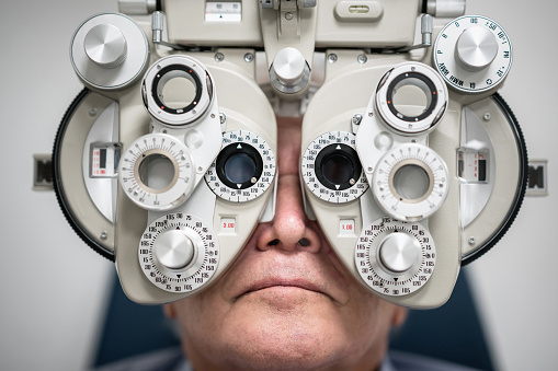 Portrait of a senior patient getting an eye exam at the optician on the phoropter - medical concepts