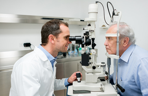 Male senior adult at the optician getting an eye exam - healthcare and medicince concepts