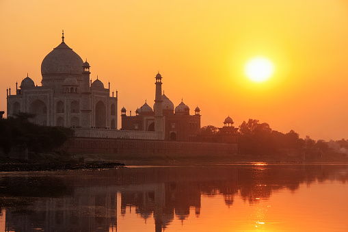 Taj Mahal reflected in Yamuna river at sunset in Agra, India. It was commissioned in 1632 by the Mughal emperor Shah Jahan to house the tomb of his favourite wife Mumtaz Mahal.