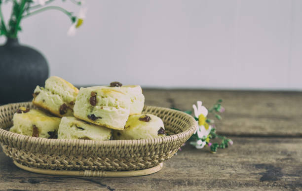 伝統的な英国菓子: スコーン。素朴な木のテーブル上のバスケットの自家製レーズンのスコーン。午後の紅茶、クリーム ティー、シャイア デヴォンやコーンウォール スタイルのハイティー� - cornish cream tea ストックフォトと画像