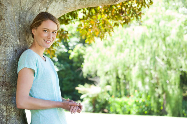 istock Happy woman leaning against the tree at park 692409504