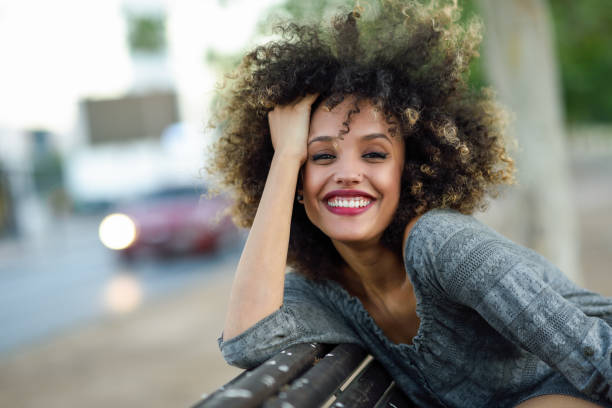 若い都市の背景に笑みを浮かべてアフロの髪型で女性を黒します。 - women smiling beautiful brown hair ストックフォトと画像