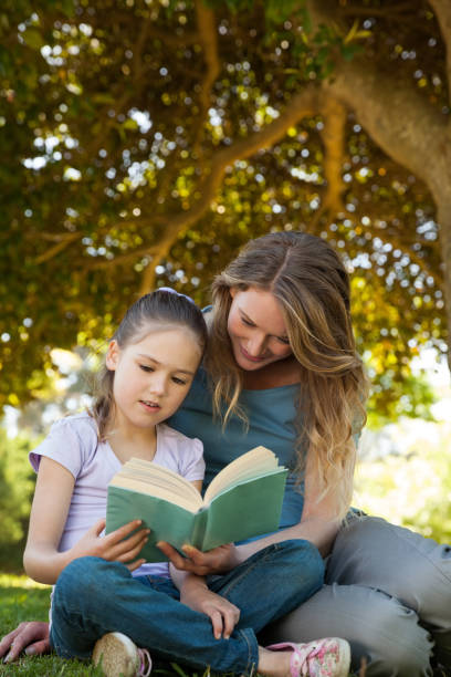 istock Mother and daughter reading a book at park 692415586