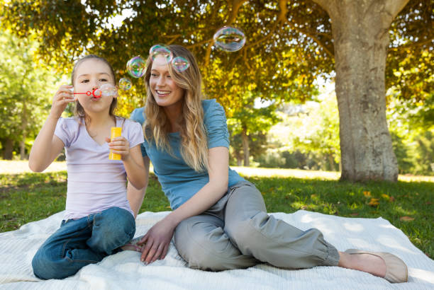 istock Mother with her daughter blowing soap bubbles at park 692444446