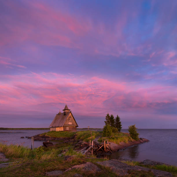 Old Russian Orthodox Wooden Church In The Village Rabocheostrovsk, Karelia. Fake Wooden Church On The Shore Of The White Sea. Rabocheostrovsk, Karelia, Russia. Northern Russia. The Village Rabochestrovsk (Town Of Kem) - View Of The Church noche blanca en la costa del mar blanco. aldea rabocheostrovsk, república de karelia.old ruso ortodoxo iglesia de madera en una isla de la piedra con el fondo de cielo rosa después de tormenta severa. famoso lugar donde filmó la película