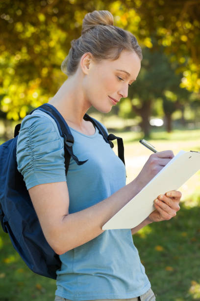 istock Beautiful young woman writing on clipboard at park 692448622