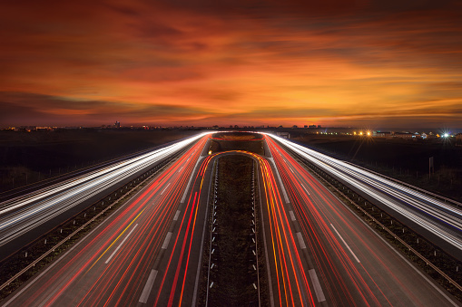 Driving on highway at dusk towards the city lights. Light trails on motorway at beautiful sunset, long exposure image.