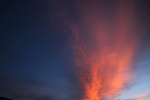 Storm clouds, their bellies ablaze with the furious red and gold of sunset, stand defiant beneath the encroaching void of night, a canvas devoid of all but the promise of impending darkness.