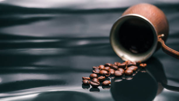 Coffee beans over black Small copper coffee pot lying on black reflective background. Scattered roasted coffee beans. Selective focus frangula alnus stock pictures, royalty-free photos & images