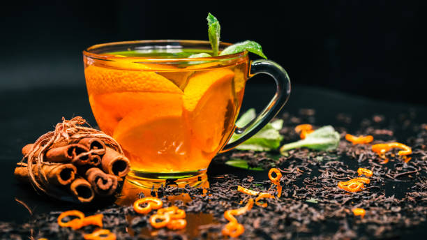 Orange tea and mint Orange tea in transparent cup with fresh mint and cinnamon sticks on glossy black background covered with dried black tea. Selective focus frangula alnus stock pictures, royalty-free photos & images