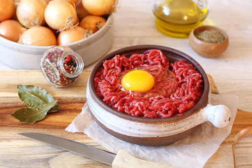 Raw minced meat with egg in ceramic pot, olive oil, seasoning and onions