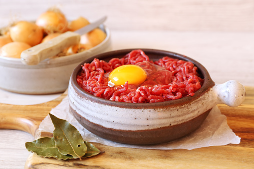 Raw minced meat with egg in ceramic pot and onions