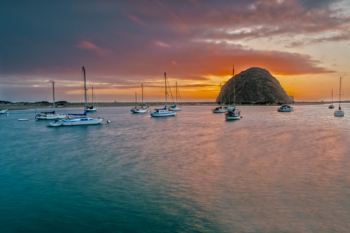 Morro Rock at Morro Bay at the Highway 1 in California. The Sun goes down and some Boats are laying in the Bay.