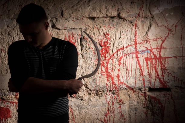 istock Man holding a sickle standing near blood stained wall 692526322