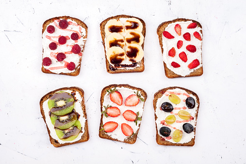 Toasts for healthy breakfast. Sweet sandwiches with cream cheese and fresh berries and fruit on white background. Top view