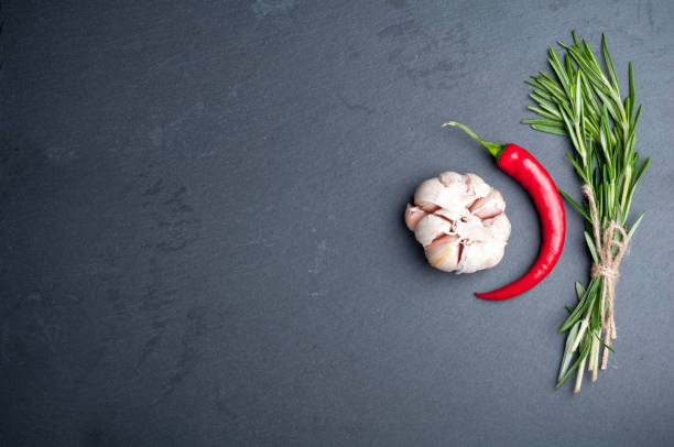 Spices background with copy space. Rosemary, chilli pepper and garlic on a dark stone background. Top view