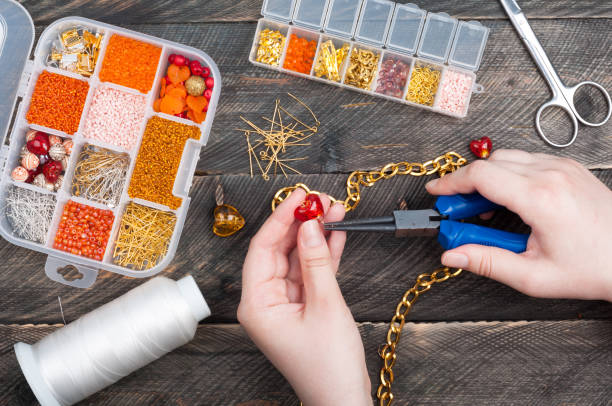 mujer haciendo joyería hecha a mano. accesorios hechos a mano. caja con perlas, corazones de vidrio, accesorios para costura en el fondo de madera vieja. vista superior - costume jewelry fotografías e imágenes de stock