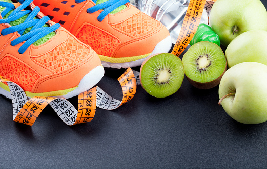 Sport shoes, fruits,  bottle of water and measuring tape on dark background. Sport equipment. Concept healthy life, sports and diet. Selective focus