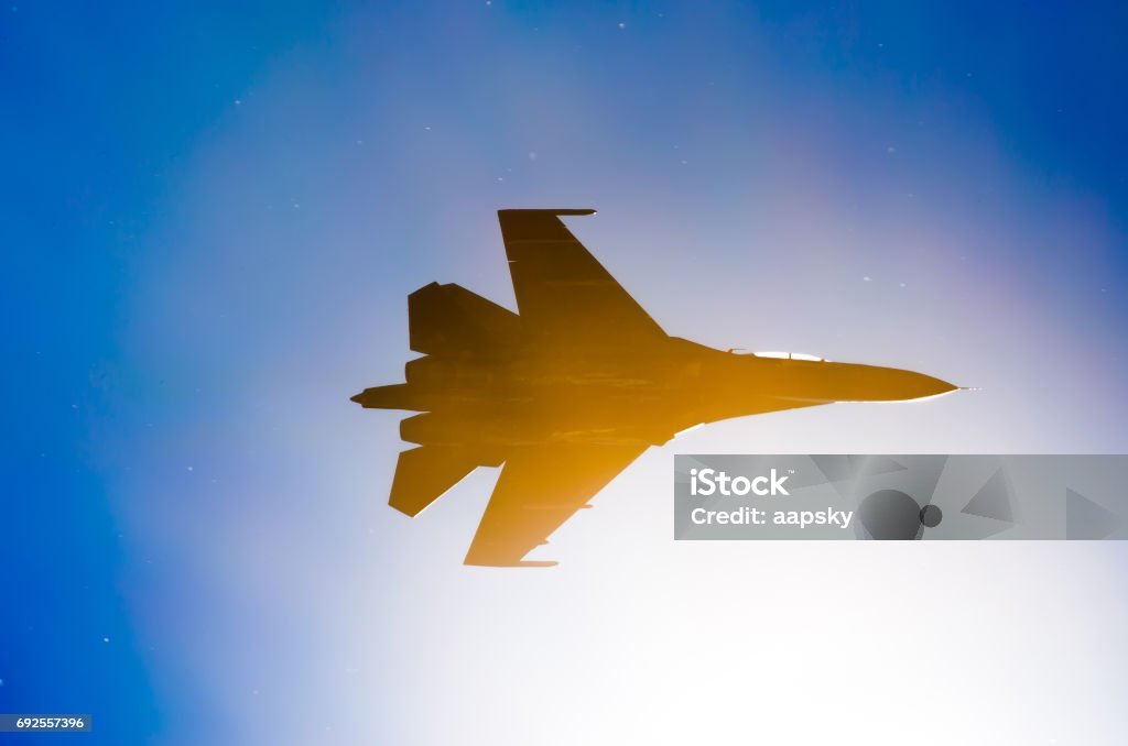 Silhouette of a military fighter sun lights blue sky. Silhouette of a military fighter sun lights blue sky Battle Stock Photo