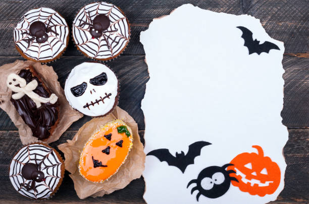 istock Halloween background. Halloween cupcakes decorated with icing on old wooden background. Burn paper and halloween decorations. Lots of copyspace. Top view 692560404
